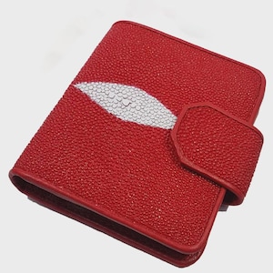 May include: A red leather notebook with a white stingray design. The notebook has a textured surface and a flap closure. The edges are neatly finished, and the overall design is sleek and stylish. This notebook is perfect for taking notes or journaling.