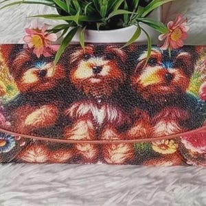 Op de afbeelding: Een rechthoekige portemonnee met een levendige print in wandtapijstijl van drie Yorkshire Terriërs omringd door kleurrijke bloemen. De portemonnee heeft een gestructureerde klepsluiting met een roze-bruine rand en een textuurrijk oppervlak.