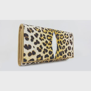 Op de afbeelding: Een rechthoekige portemonnee met een luipaardprint in tinten beige, bruin en zwart. De portemonnee heeft een wit, druppelvormig designelement en is afgewerkt met een lichtbruine rand.