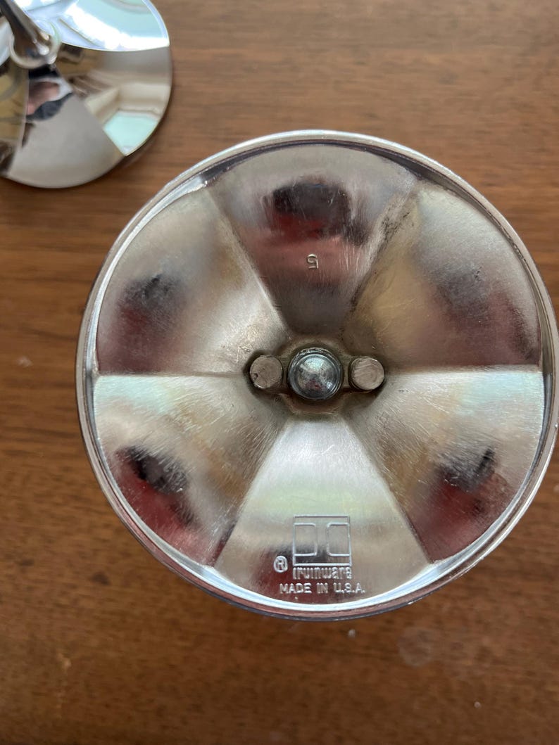 May include: Close-up of a silver metal object with a circular base and a central, rounded post. The base is divided into six sections. The text "IRWINWARE MADE IN U.S.A." is visible. The number "5" is stamped on the object.