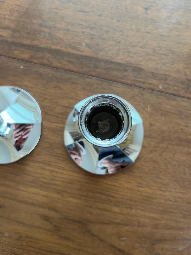 May include: Close-up of two shiny, silver bottle stoppers. The stoppers have a faceted design on the top and a cylindrical base. The stoppers are on a wooden surface.