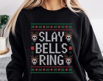 Könnte beinhalten: Schwarzes Sweatshirt mit festlichem Design. Das Design zeigt den Text "SLAY BELLS RING" in Weiß, umgeben von grünen und roten Weihnachtsmustern und Totenkopf-Rentier-Grafiken. Ein gemütlicher und stilvoller Weihnachts-Pullover.