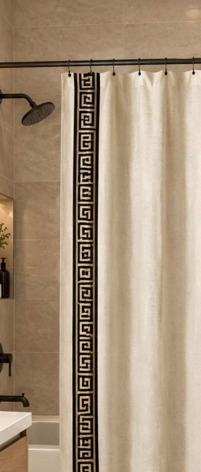 May include: A beige shower curtain featuring a vertical black and gold Greek key pattern border along the side. The curtain is suspended from a dark metal rod with matching rings, displaying a textured fabric finish throughout the panel.