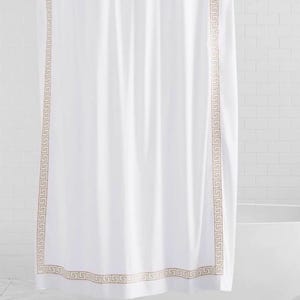 May include: A white shower curtain featuring a vertical and horizontal border with a tan-colored Greek key pattern. The curtain hangs from a circular metal rod and is made of a smooth fabric that drapes in soft, vertical folds.