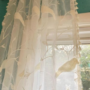 Pu&ograve; includere: Un pannello per tenda bianco trasparente con un motivo a vite ricamato e uccelli in rilievo testurizzati. Il tessuto &egrave; leggero e traslucido, arricchito da piccole nappe decorative lungo il bordo verticale, appeso a un bastone per tende.