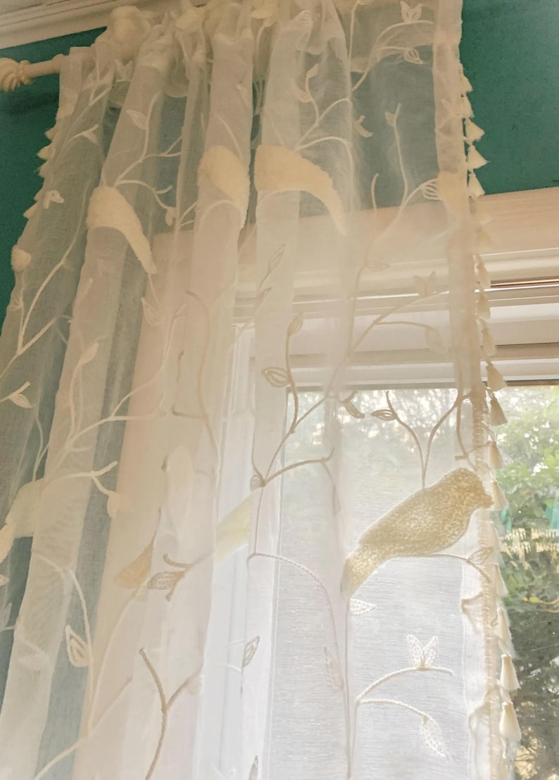 Pu&ograve; includere: Un pannello per tenda bianco trasparente con un motivo a vite ricamato e uccelli in rilievo testurizzati. Il tessuto &egrave; leggero e traslucido, arricchito da piccole nappe decorative lungo il bordo verticale, appeso a un bastone per tende.