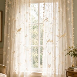 Pu&ograve; includere: Una coppia di tende trasparenti color bianco sporco con delicati motivi a vite ricamati e piccoli uccelli appollaiati sui rami. I bordi delle tende sono rifiniti con una frangia decorativa e sono appese a un bastone per tende dorato.