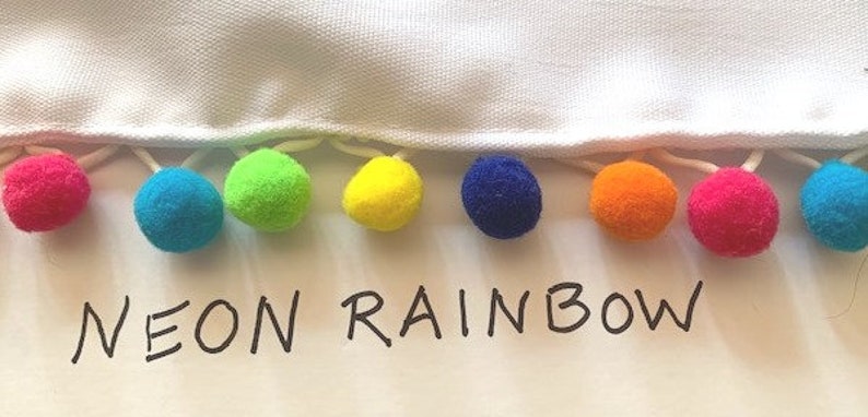 May include: A white fabric edge trimmed with a row of small, round, multi-colored pom-poms in shades of pink, blue, green, yellow, dark blue, orange, and magenta. The text NEON RAINBOW is printed in black capital letters below the pom-pom trim.