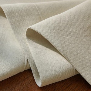 May include: Close-up of a light beige fabric with a textured surface. The fabric is folded over itself, showing the soft, smooth texture.