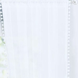 May include: White sheer curtain with a white pom-pom trim along the edges.