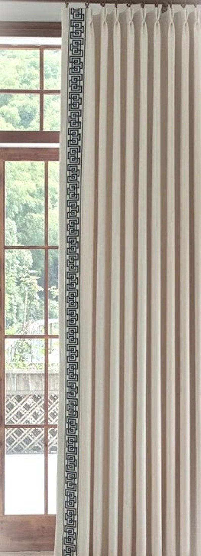May include: White curtains with a black geometric pattern border. The curtains are hanging in a window with a wooden frame.