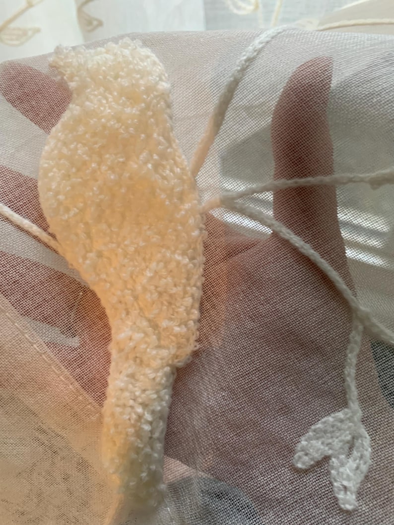 Pu&ograve; includere: Una tenda in tessuto bianco semitrasparente con un motivo a uccello ricamato in rilievo color bianco sporco. Il design include delicati dettagli in filo bianco che si estendono dalla forma dell'uccello, formando linee sottili e una piccola foglia.