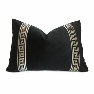 May include: Black rectangular pillow with a silver Greek key design border on each side. The pillow has a soft, velvety texture and a classic, elegant style. The design is symmetrical and centered.