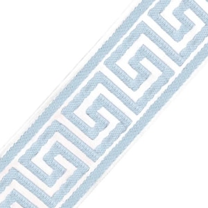 May include: A strip of fabric trim featuring a repeating light blue Greek key pattern embroidered onto a solid white background. The design consists of continuous interlocking geometric lines that run diagonally across the length of the trim.