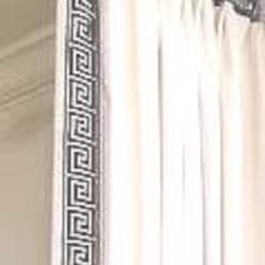 May include: A cream-colored curtain hangs from a metallic rod with decorative finials. The curtain features a prominent vertical border along the leading edge, decorated with a repeating black and white Greek key geometric pattern.