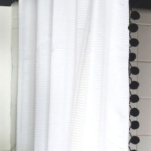 May include: White shower curtain with a black pom-pom trim.