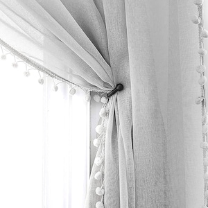 May include: White sheer curtains with a pom-pom trim and a black curtain tieback.