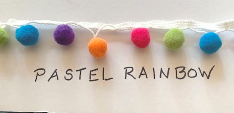 May include: A white woven trim featuring a series of small, fuzzy pom-poms in various colors including lime green, bright blue, purple, orange, and hot pink. The text "PASTEL RAINBOW" is written in black ink below the colorful pom-pom trim.