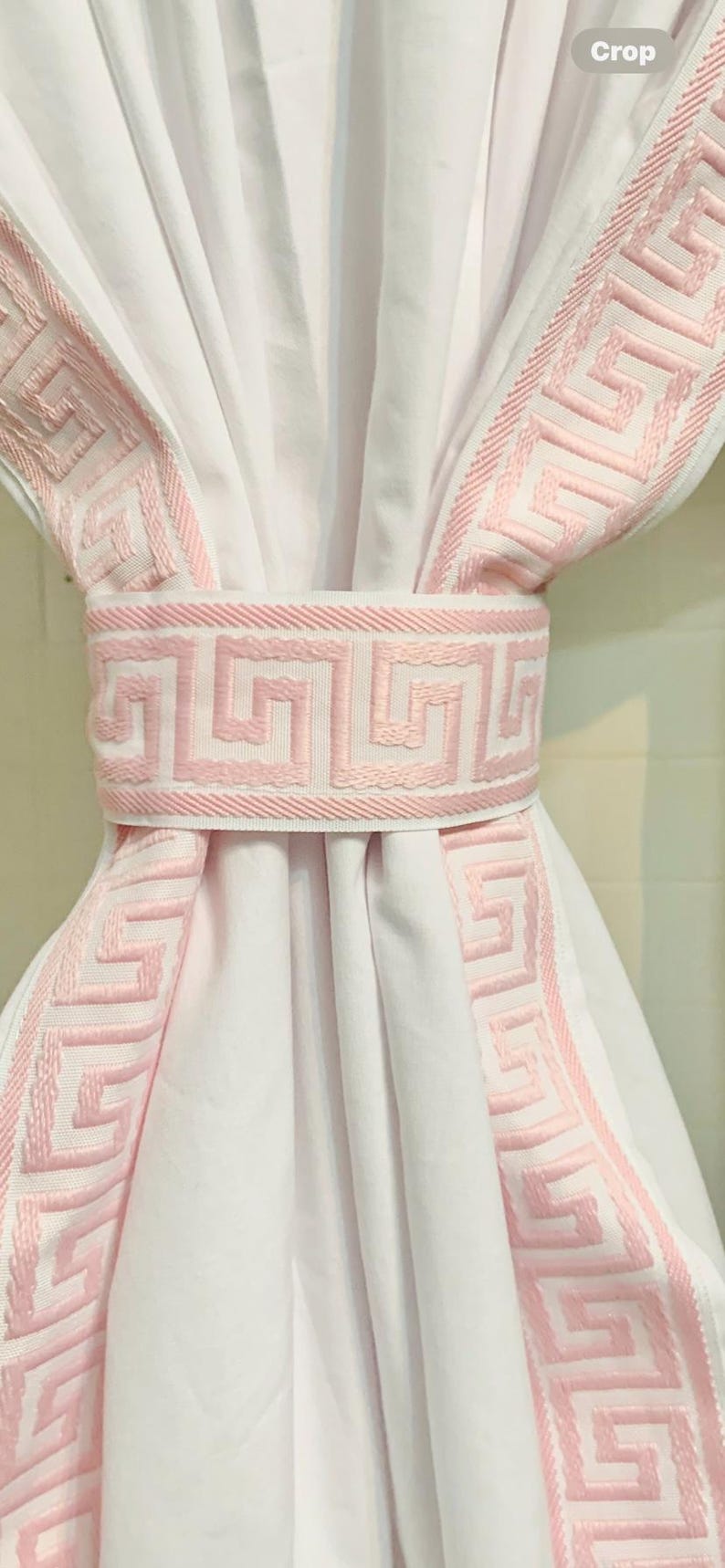 May include: A white curtain panel gathered in the center by a matching tieback. The curtain and tieback feature a wide, light pink embroidered trim with a repeating geometric Greek key pattern along the edges and the center band.