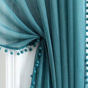 May include: Teal sheer curtains with a pom-pom trim. The curtains are gathered at the top and tied back with a matching ribbon.