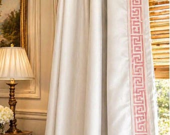 May include: A floor-length off-white curtain panel featuring a vertical border with a pink Greek key pattern. The curtain is suspended from a gold-toned metal rod with decorative finials, showcasing a pleated header and smooth fabric.