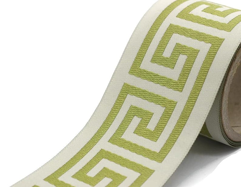 May include: A roll of woven ribbon featuring a repeating lime green Greek key pattern on a cream-colored background. The ribbon has a textured surface and is wound around a cardboard spool, displaying a continuous geometric design.