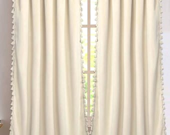 Può includere: Una coppia di tende per finestra color bianco sporco con tasca per bastone e file verticali di piccole nappe in tessuto abbinate lungo i bordi interni ed esterni. Le tende cadono dritte, creando morbide pieghe verticali sulla superficie.