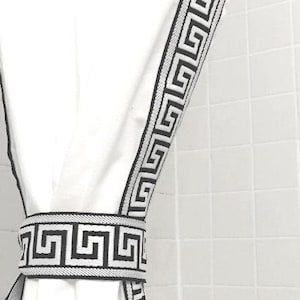 May include: A white curtain panel featuring a black Greek key pattern trim along the vertical edge, secured by a matching white and black Greek key patterned tieback, creating a clean and structured look for window treatments.