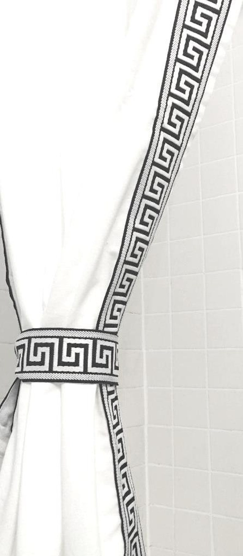 May include: A white curtain panel featuring a black Greek key pattern trim along the vertical edge, secured by a matching white and black Greek key patterned tieback, creating a clean and structured look for window treatments.