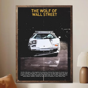 Puede incluir: Un póster enmarcado con un coche deportivo blanco dañado sobre un fondo oscuro. El título "THE WOLF OF WALL STREET" está en amarillo en la parte superior. El póster tiene un estilo vintage, con marco de madera.