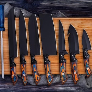 May include: A collection of eight black kitchen knives with wooden handles, decorated with blue and orange patterns, displayed on a wooden chopping board. A blue-handled screwdriver is to the left of the knives.