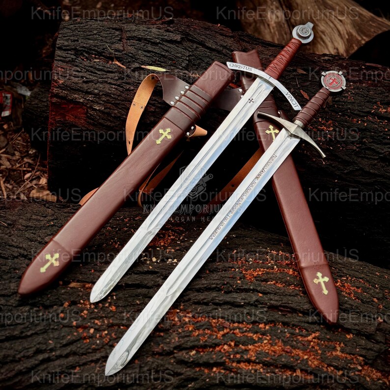 May include: Two medieval swords with silver blades and brown leather-wrapped handles rest on a wooden surface. Each sword is accompanied by a brown leather sheath adorned with a gold cross. The swords have inscriptions.