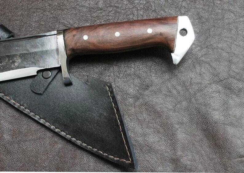 May include: Close-up of a hunting knife with a dark wooden handle and a silver bolster. The blade is partially visible, and the knife rests in a black leather sheath with white stitching. The handle has three white dot inlays.