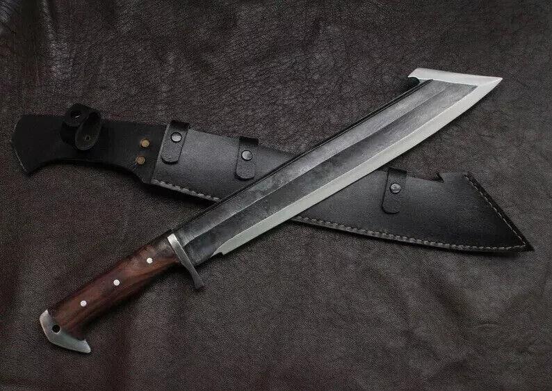 May include: A large, silver-bladed knife with a dark wooden handle and a black leather sheath. The knife has a unique, angled blade design and is resting on a textured, dark surface. The sheath has a belt loop.