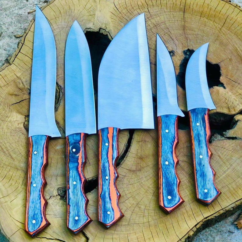 May include: A collection of six stainless steel knives with blue and orange wooden handles. The blades are of different shapes and sizes, including a large cleaver. The handles have a textured design and are secured with white rivets. The knives are displayed on a wooden surface.