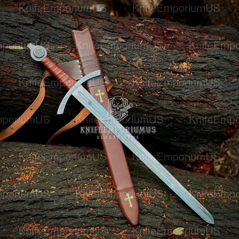 May include: A medieval sword with a silver blade and a brown leather-wrapped handle rests on a log. The sword is in a brown leather sheath with a cross emblem. The word "CHRISTUS" is inscribed on the blade.