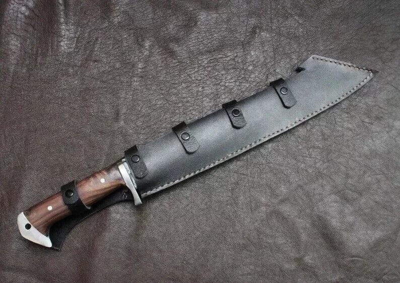 May include: A large hunting knife with a wooden handle and a black leather sheath. The knife blade is partially visible, and the sheath has three straps with buckles. The handle has a silver bolster.