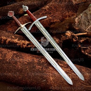 May include: Two medieval swords with silver blades and brown handles rest on a bed of wood. One sword has the word "VINCIT" on the blade, and the other has "CHRISTUS". The swords have ornate crossguards and pommels.