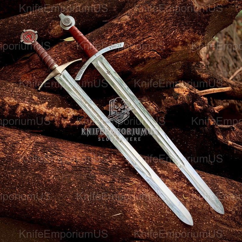 May include: Two medieval swords with silver blades and brown handles rest on a bed of wood. One sword has the word "VINCIT" on the blade, and the other has "CHRISTUS". The swords have ornate crossguards and pommels.