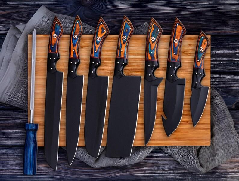 May include: A collection of eight black kitchen knives with wooden handles, decorated with blue and orange patterns, presented on a wooden board. Includes a sharpening steel. Knives vary in size and shape.