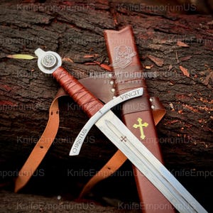 May include: A medieval sword with a brown leather-wrapped handle and a silver blade. The sword is displayed with its brown leather sheath, which has a gold cross emblem. The word "CHRISTUS" is etched on the blade.