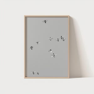 Puede incluir: Una impresión enmarcada que presenta una bandada de pájaros en vuelo contra un fondo gris apagado. Las aves están representadas en tonos grises y blancos, creando una estética minimalista y serena. La obra de arte está encerrada en un marco de madera de color claro.