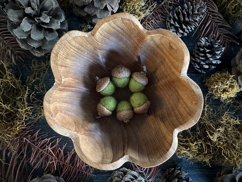 Pu&ograve; includere: Una ciotola di legno con un bordo a festoni, piena di sei ghiande di feltro verde.