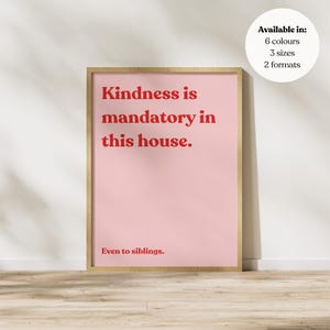 May include: A framed pink poster with the text "Kindness is mandatory in this house. Even to siblings." in red. A white circle in the upper right corner states "Available in: 6 colours, 3 sizes, 2 formats."