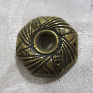 Puede incluir: Un botón decorativo de metal dorado con un diseño geométrico y un agujero central.