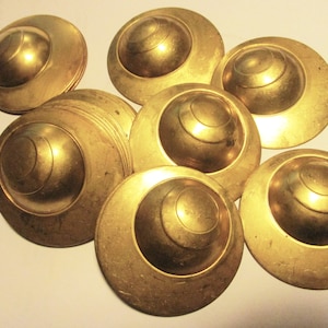 Puede incluir: Un grupo de nueve discos de metal de color dorado con un centro elevado y redondeado. Los discos tienen un acabado liso y brillante y parecen ser decorativos.