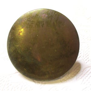 May include: A round, brass-colored button with a smooth, slightly textured surface.
