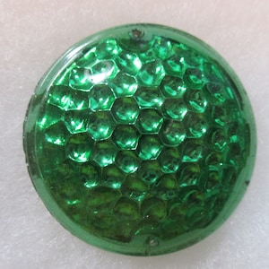 May include: A round, green, reflective lens with a honeycomb pattern. The lens is made of glass and has a smooth, shiny surface.