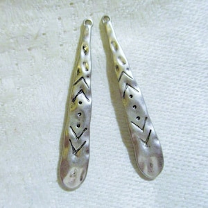 May include: Two silver metal earring pendants with a hammered texture and a geometric design. The design features a series of triangles and dots.