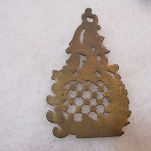 以下が含まれることがあります： 繊細で複雑なデザインの金色の金属製の装飾品。装飾品の中央には円形の模様があり、縁には花のような模様が施されています。